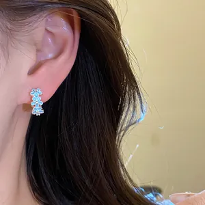 Close-up view of blue enamel flower hoop earrings worn by a model with dark hair.