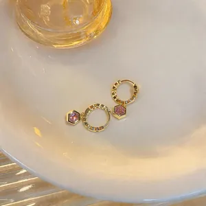 Close-up of elegant gold hoop earrings with hexagonal pink zircon dangles