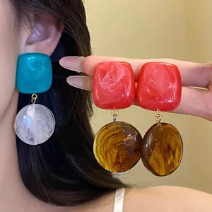 Gros plan de boucles d'oreilles pendantes en résine avec contrastes de couleurs géométriques.