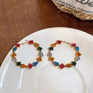 Detailed macro shot of colorful square and teardrop zircon hoop earrings on white plate.
