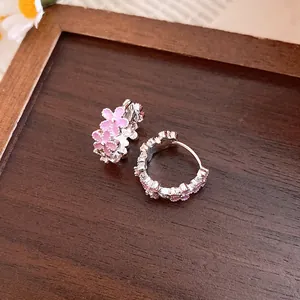 Detailed view of silver hoop earrings featuring delicate pink enamel flowers on wood