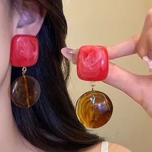 Vue détaillée de boucles d'oreilles pendantes en résine rouge et ambre style rétro.