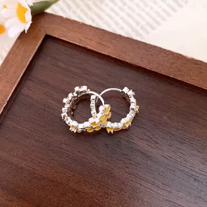 Detailed close-up of sweet floral hoop earrings with yellow enamel daisy patterns.