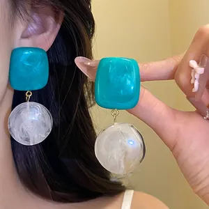 Gros plan de boucles d'oreilles pendantes en résine sarcelle et blanche sur un modèle