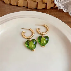 Elegant 24k gold plated hoop earrings with green glass heart charms on a plate