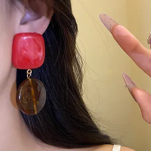 Gros plan de boucles d'oreilles rétro en résine rouge et ambre sur l'oreille.