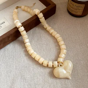 Dettaglio di una collana in acrilico crema con perline cilindriche e grande ciondolo a cuore.