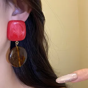 Gros plan d'un mannequin portant des boucles d'oreilles en résine rouge et ambre rétro