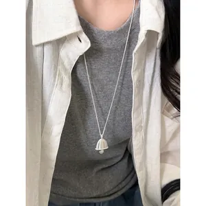 Detailed view of a minimalist silver oval bell pendant necklace styled with a gray sweater