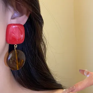 Gros plan détaillé sur des boucles d'oreilles en résine rouge et ambre portées par un mannequin