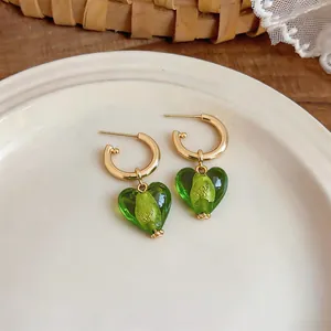 Detailed macro view of heart-shaped green earrings with 24k gold plating on a white plate