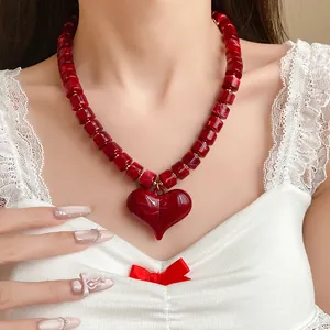 Dettaglio di una collana di perle acriliche rosse con un grande ciondolo a cuore lucido.