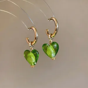 Detailed view of green glass heart pendants on gold hoop earrings with silver needles