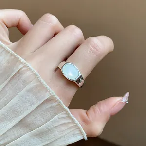 Vista detallada de un anillo abierto con resina blanca ovalada usado en una mano elegante
