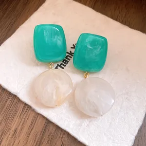 Gros plan de boucles d'oreilles rétro en résine bicolore vert et blanc sur carte