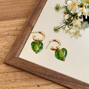 Close-up of green heart-shaped glass pendants on gold hoop earrings in reflective setting