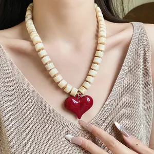 Primo piano di un grande ciondolo a cuore rosso su una collana di perle cilindriche bianco panna.