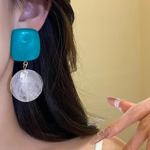 Détail rapproché de boucles d'oreilles pendantes en résine géométrique sarcelle et blanc