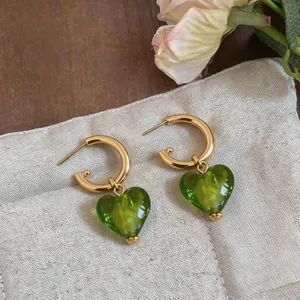 Detail of gold-plated C-hoop earrings with elegant green heart-shaped glass pendants.