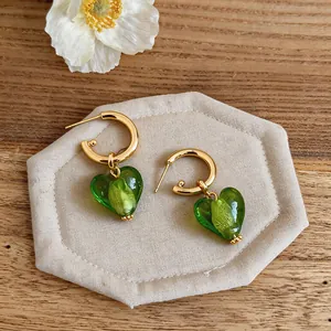Close-up of gold hoop earrings with translucent green heart-shaped glass charms