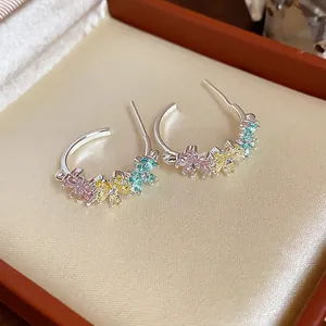 Close-up detail of C-shaped earrings with colorful zircon flower clusters.