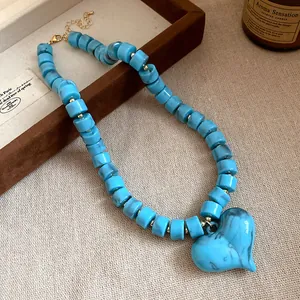 Dettaglio della collana con perle acriliche marmorizzate blu e ciondolo a cuore su tessuto.