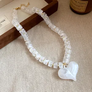 Dettaglio di perle acriliche marmorizzate bianche e grande ciondolo a cuore su collana