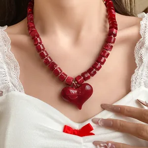 Primo piano di collana di perle acriliche rosse con grande ciondolo a cuore.