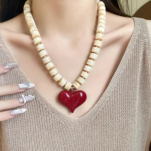 Dettaglio di una collana di perle acriliche con un grande ciondolo a cuore rosso lucido