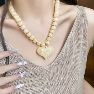Dettaglio di un'elegante collana con ciondolo a cuore in acrilico e perline quadrate.