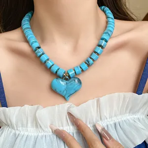 Dettaglio di una collana di perle acriliche turchesi con ciondolo a cuore su una modella