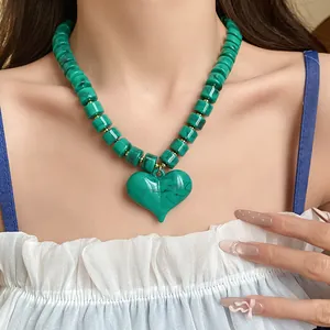 Dettaglio di una collana con ciondolo a cuore in acrilico verde indossata da un modello