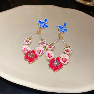 Close-up of vintage enamel floral drop earrings with pearls and butterfly details