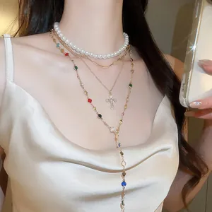 Close-up detail of a multi-layered gold necklace with pearls and rhinestone cross