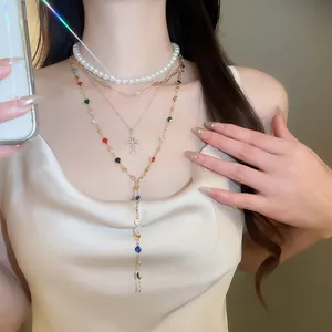 Detail shot of multi-layered gold necklace with pearls, cross pendant, and colorful gems