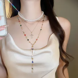 Close-up of a layered necklace with resin pearls and a rhinestone cross pendant