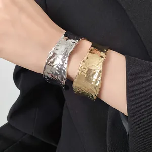 Primer plano de brazaletes abiertos arrugados en oro y plata en la muñeca de una modelo