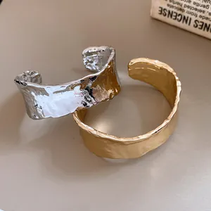 Detalle macro que muestra la textura arrugada irregular de los brazaletes en oro y plata.