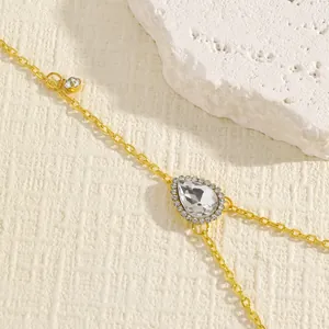 Close-up of a gold-tone body chain with a large teardrop rhinestone and intricate pavé