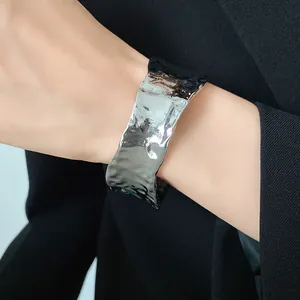 Primer plano de un brazalete abierto minimalista plateado con textura arrugada en muñeca