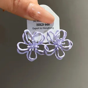Primer plano de pendientes de flores huecas lavanda con acabado de aceite mate.
