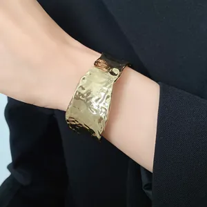 Detalle del brazalete abierto dorado martillado en la muñeca con elegante textura arrugada