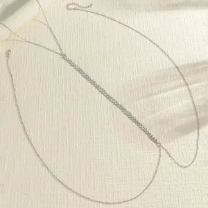 Detail view of silver vintage body chain with textured pattern on beige surface.
