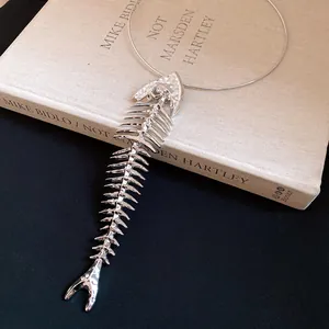 Detailed view of a silver fishbone pendant with rhinestones on a thin wire choker necklace.