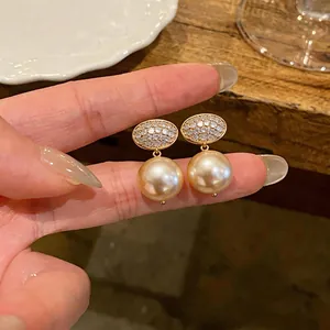 Close-up of French-style oval zircon and champagne pearl drop earrings on fingers