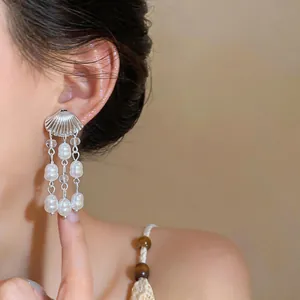Gros plan de boucles d'oreilles en argent en forme de coquillage avec glands de perles