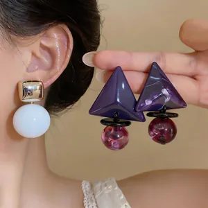 Dettaglio di orecchini geometrici in resina con forme quadrate dorate e triangoli viola