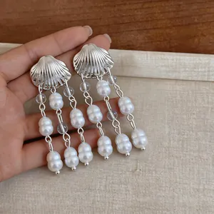 Gros plan de boucles d'oreilles argentées en forme de coquillage avec glands de perles.