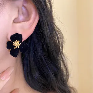 Close-up of black velvet flower earring with golden stamen detail on model's ear.