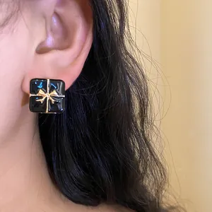 Close-up of elegant black square gift box stud earring featuring a delicate gold bow design
